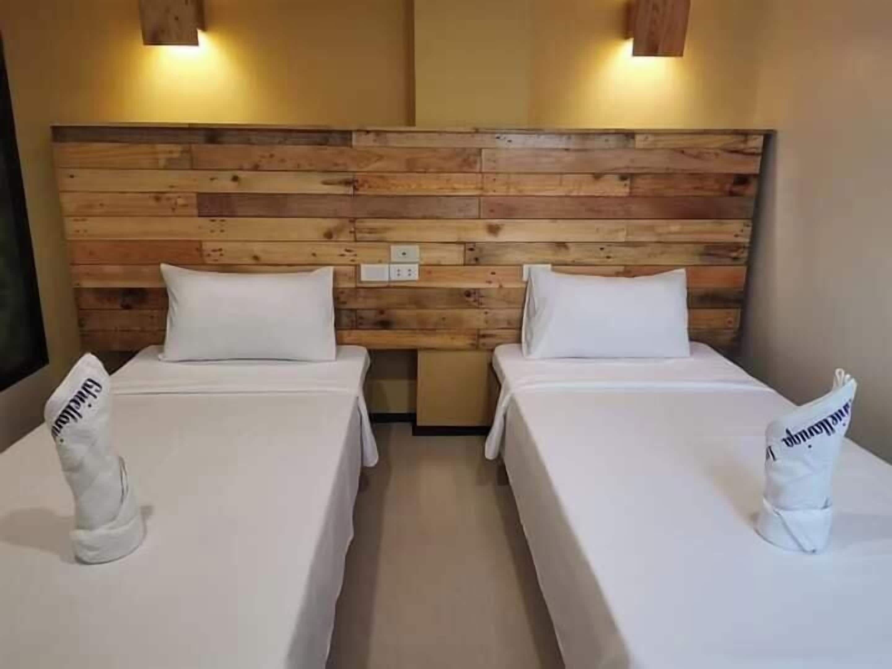 Two single beds with wooden headboards and white bedding, a small table between them, and a wall-mounted light fixture.
