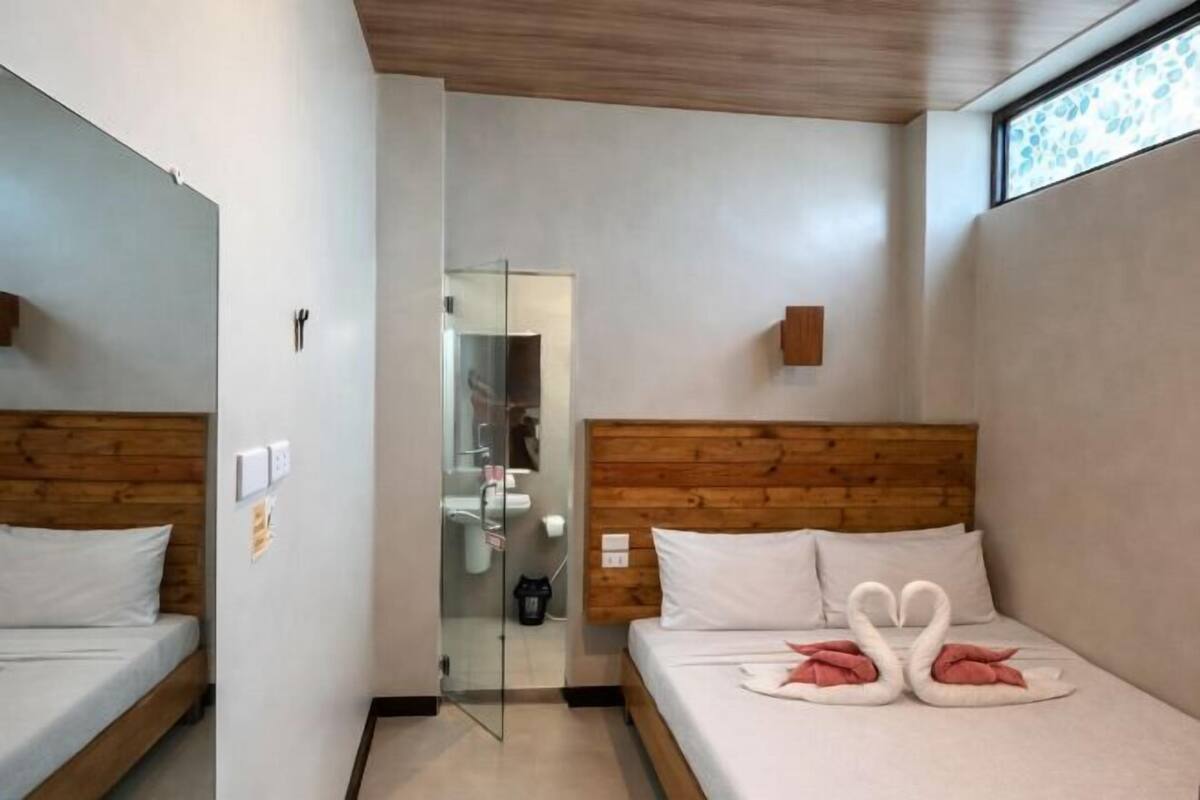 A hotel room with two beds, a wooden headboard, a glass partition, and a window with a view.
