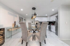 A modern kitchen with white cabinets, a glass dining table, and two chairs. - 3-Bed apartment with Sunset Sea Views, Blouberg (Cape Town)