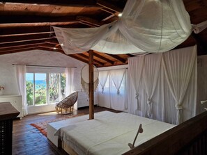 A bedroom with a large bed, a wooden ceiling, and a view of the ocean.