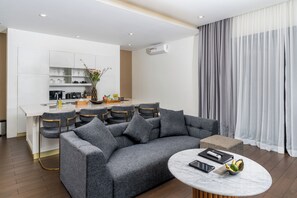 A modern living room with a grey sofa, a marble coffee table, and a kitchen area in the background. - The Claremont Luxury Villas (Seminyak)