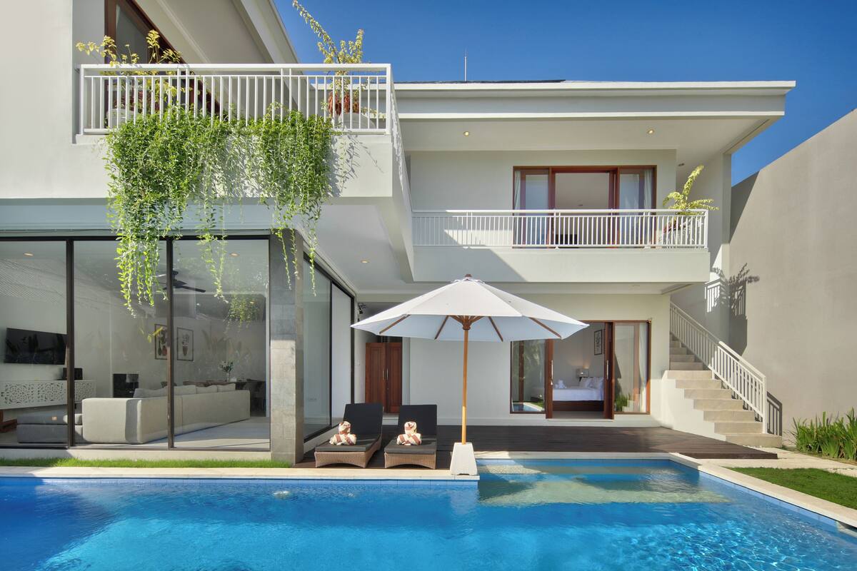 A modern two-story house with a swimming pool, outdoor seating, and a staircase leading to the upper floor.