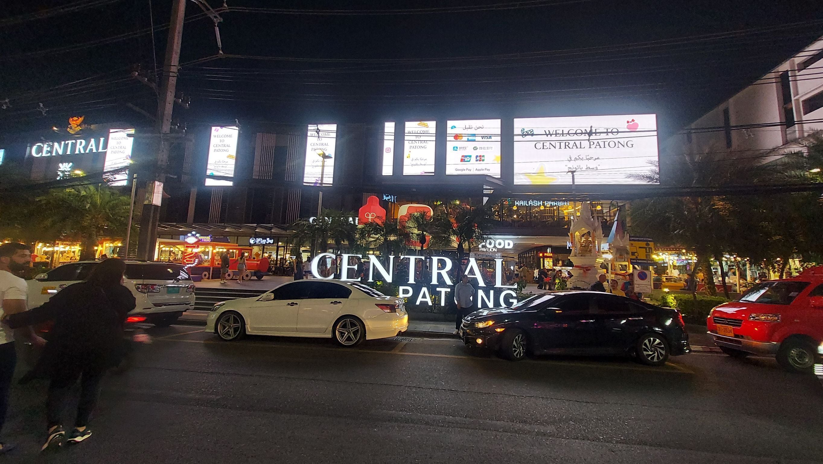 Escena de calle concurrida con un gran anuncio iluminado para Central Patong.