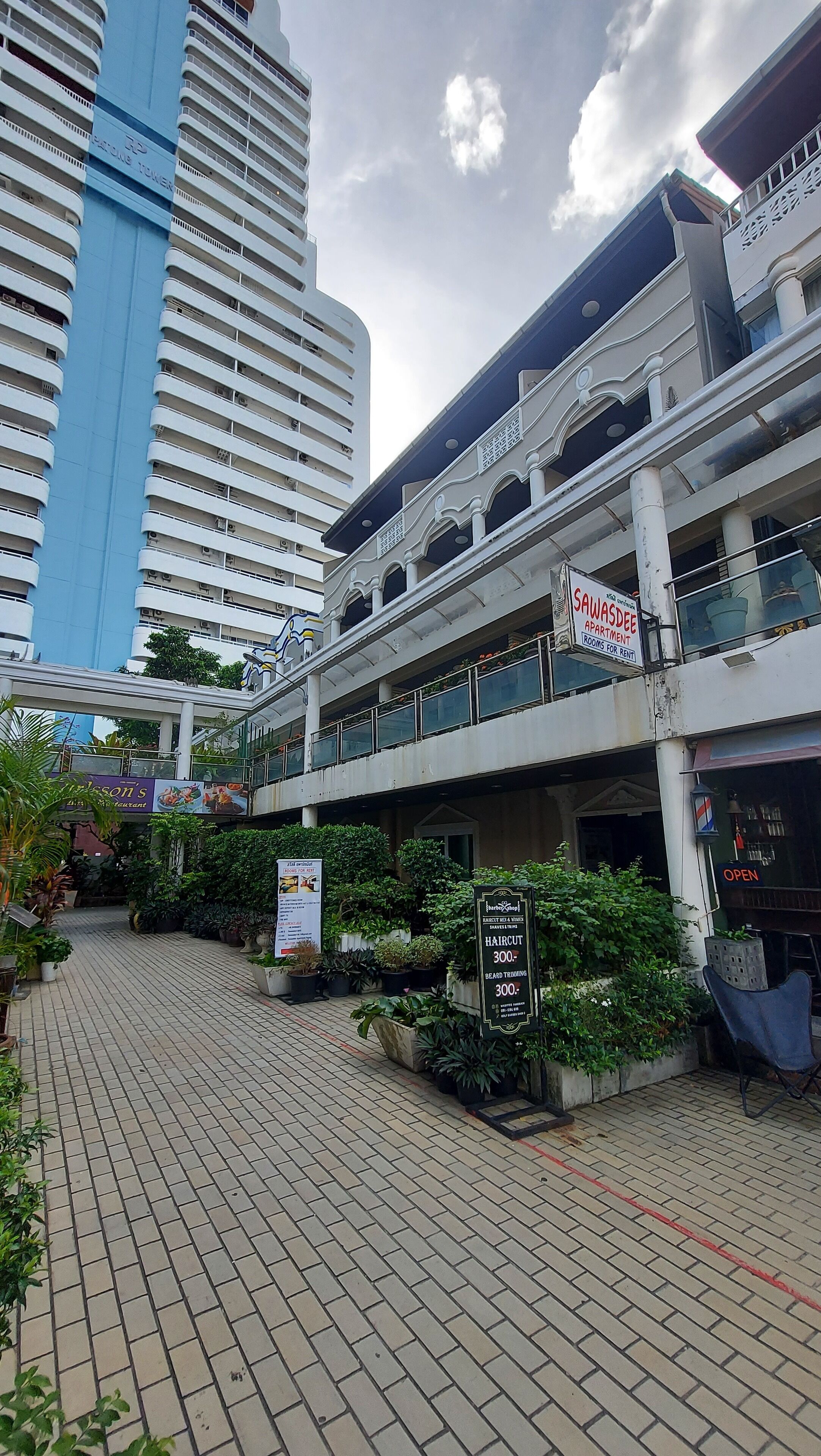 A multi-story building with a sign for 'SAWASDEE APARTMENTS' and a 'Haircut 300' sign.
