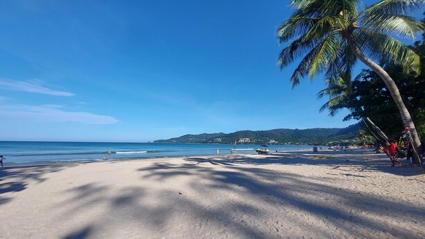 A beach with clear skies, palm trees, and a distant mountain range. - Sawasdee Apartment Patong (Patong)