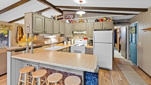 A kitchen with wooden cabinets, a central island with stools, a stove, and a refrigerator.