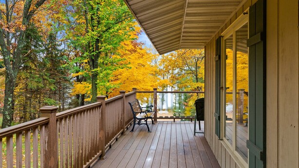 A wooden deck with a railing, two benches, and a covered porch area.