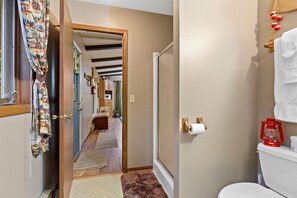 A hallway with a wooden door leading to a kitchen, a toilet with a red lantern, and a towel rack with a white towel.