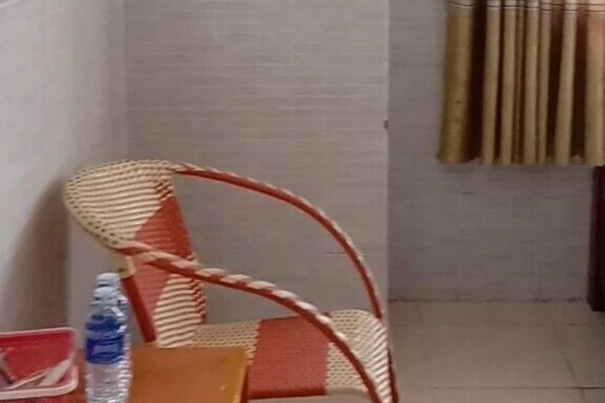 A corner room with a single chair, a table with a water bottle, and a curtain.