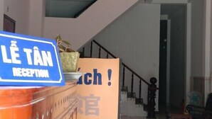 Un área de recepción con un cartel que dice "Lê Tân Reception", una escalera y un gran letrero con caracteres chinos.
