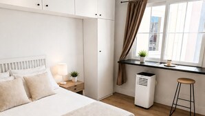 Ein modernes Schlafzimmer mit einem großen Bett, einem Schreibtisch, einem Stuhl, einem Fenster mit Vorhängen und einer Heizung.