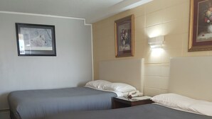 A hotel room with two single beds, a bedside table with a lamp, and framed artwork on the walls. - Alpine Lodge Motel (Grande Cache)