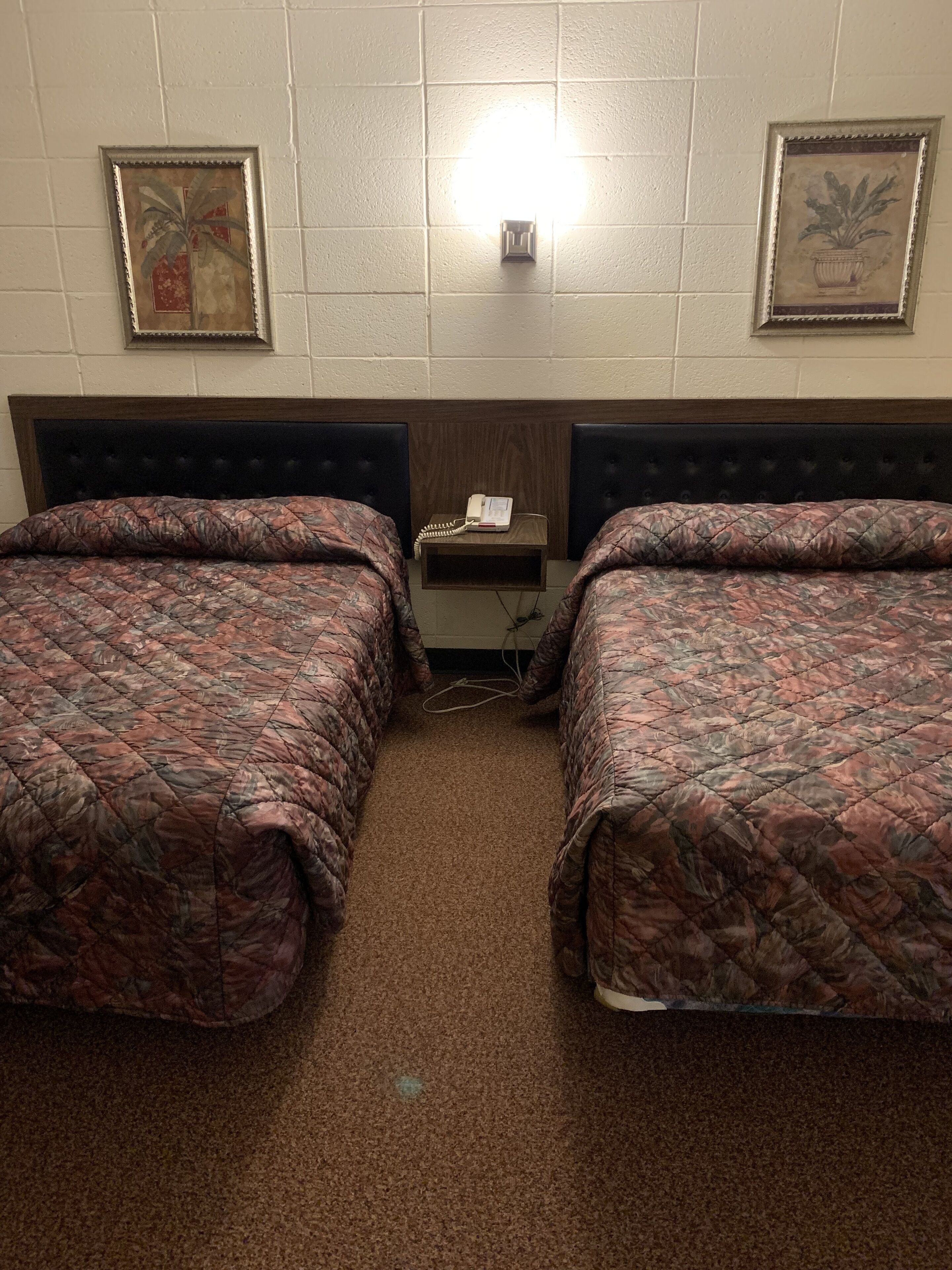 Habitación de hotel con dos camas, un pequeño escritorio con un teléfono y dos cuadros en la pared.