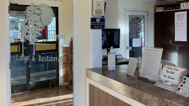 A hotel reception area with a wooden counter, framed artwork on the walls, and a sign indicating the rooming policy. - Alpine Lodge Motel (Grande Cache)
