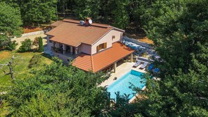 Una casa de dues plantes amb piscina, envoltada de vegetació densa.