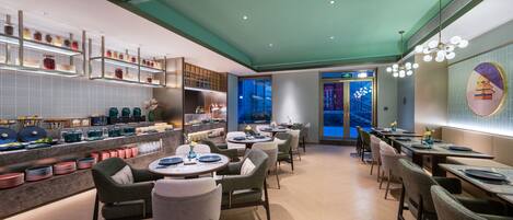A modern restaurant interior with a teal ceiling, neatly arranged tables and chairs, and a view of the cityscape through the window.