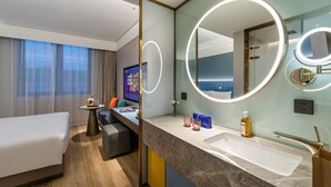 A modern hotel room with a large bed, a desk with a computer, a bathroom with a large mirror and sink, and a view of the city. - Beijing Tiananmen Qianmen Manxin Hotel (Beijing)