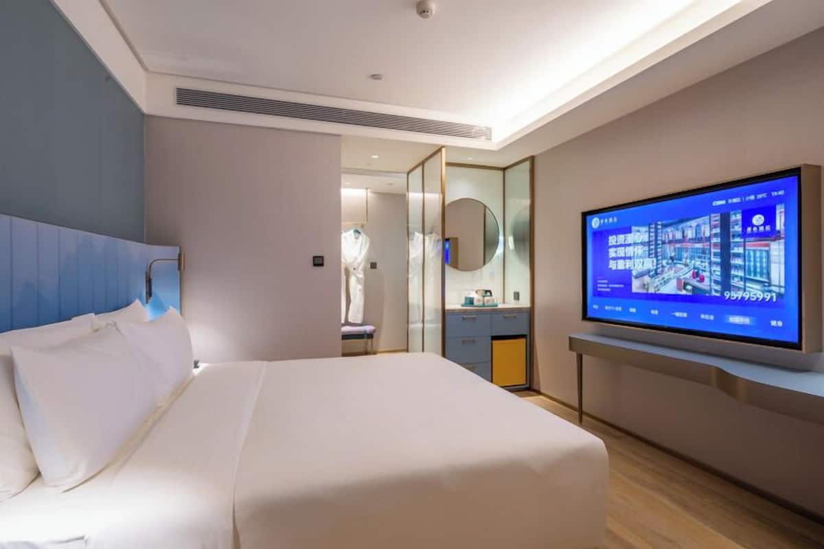 Ein modernes Hotelzimmer mit einem großen Bett, einem an der Wand befestigten Fernseher und einem Spiegel.