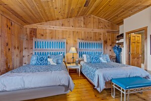 Una habitación de madera con dos camas, un banco y una mesita de noche con lámpara.