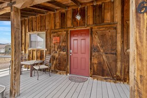 A wooden exterior with a red door, a window, and a table with chairs on a wooden deck.