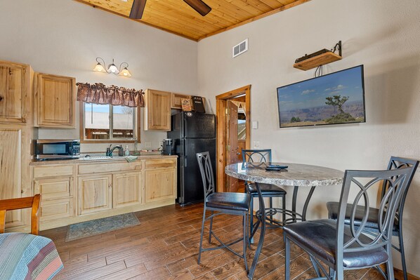 A kitchen with wooden cabinets, a black refrigerator, a dining table with chairs, and a painting on the wall. - Trapper's Rendezvous (Williams)