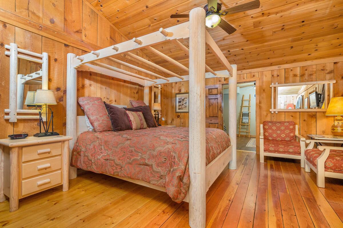 Une chambre à coucher dans une cabane en bois, avec un lit à baldaquin, un bureau avec une lampe et une chaise.