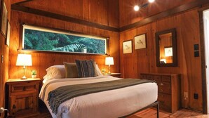 Una habitación con paneles de madera, una cama, dos lámparas de noche, un cuadro grande enmarco, un aparador y un espejo.