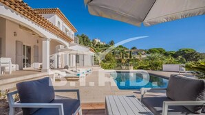 A pool area with lounge chairs and umbrellas, a tiled roof, and a view of the surrounding landscape. - Modern villa in the prestigious golf domain (STE MAXIME)