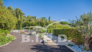 A curved driveway leading to a property with a well-maintained garden and a variety of trees and shrubs. - Modern villa in the prestigious golf domain (STE MAXIME)