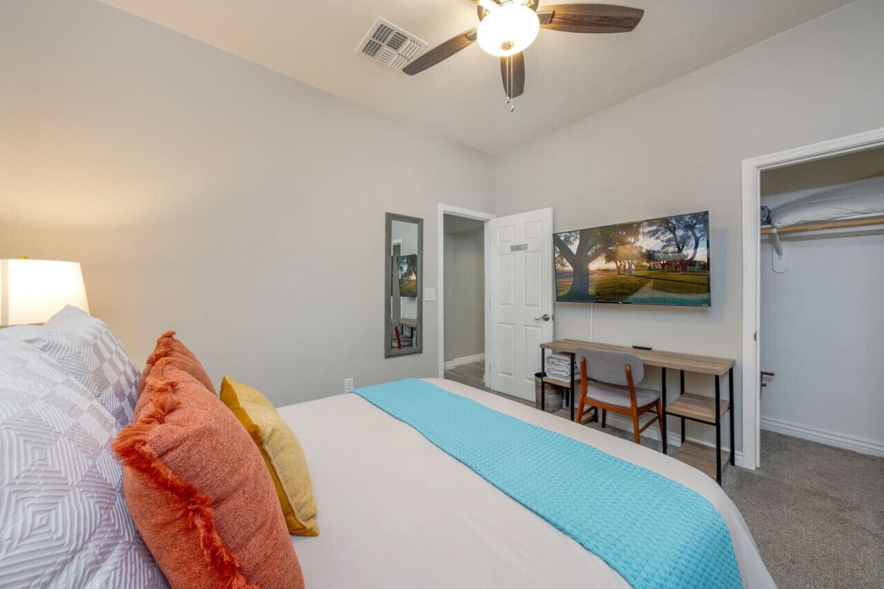 Ein Schlafzimmer mit Bett, Schreibtisch, Stuhl, Deckenventilator und einem Bild an der Wand.