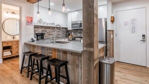 A modern kitchen with a central island, bar stools, stainless steel appliances, and wooden accents.