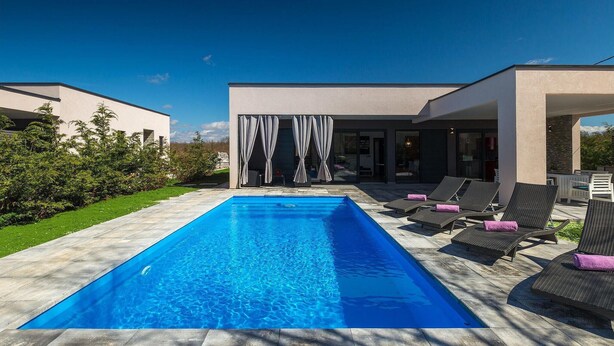 A modern outdoor swimming pool with lounge chairs and a covered patio area.