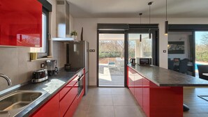A modern kitchen with red cabinetry, stainless steel appliances, and a view to an outdoor patio.