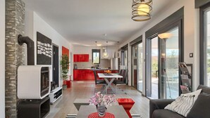 A modern living room with a fireplace, a dining area, and a kitchen with red cabinets.