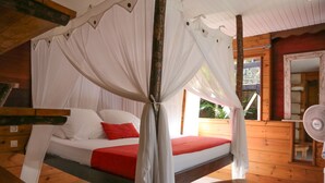 A room with a bed under a canopy, a wooden bench, and a fan.