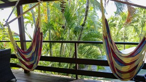 A hammock on a wooden deck with a view of palm trees.