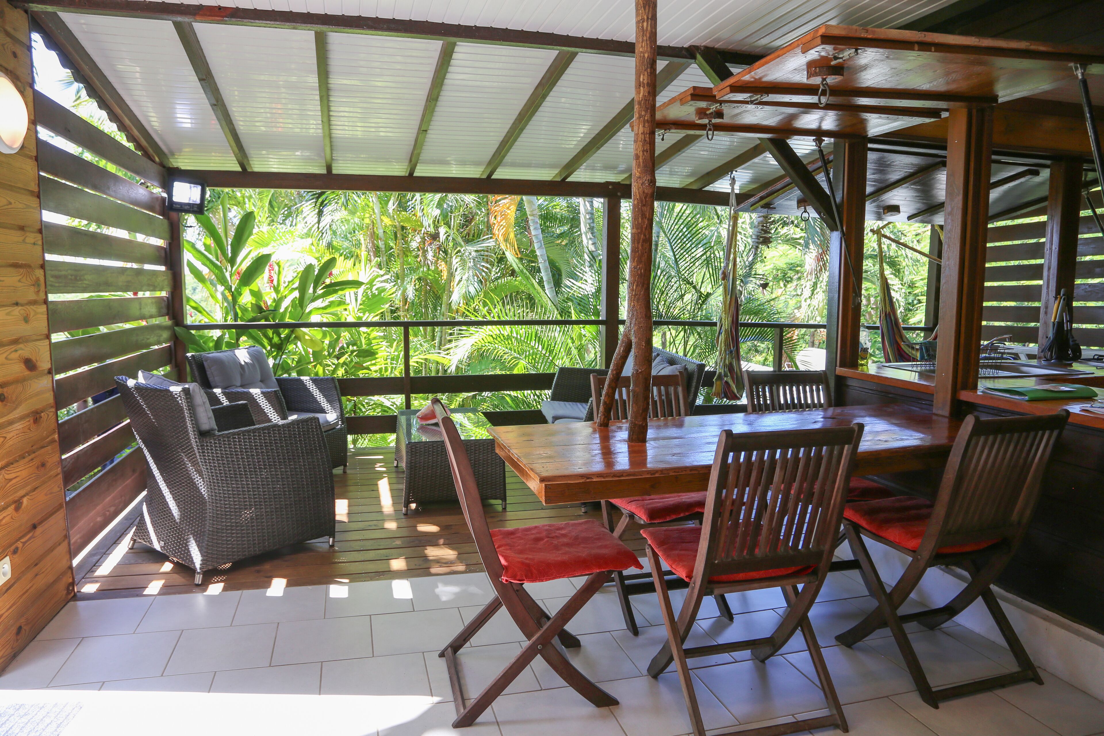 Un área de comedor al aire libre techada, con mobiliario de madera y vistas a un follaje exuberante.