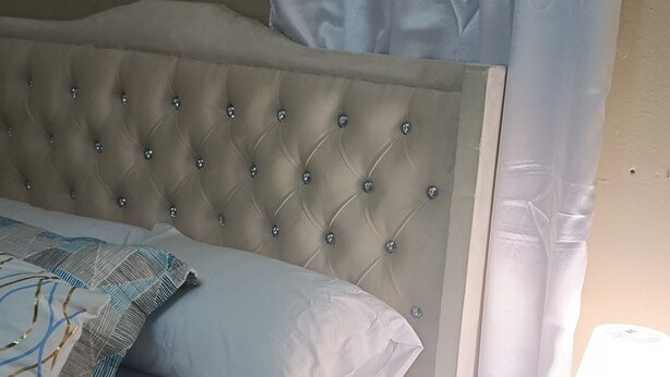 A bedroom with a tufted headboard, a bed with patterned bedding, a bedside table with a remote control, and a nightstand with drawers. - Luisandro (Punta Cana)