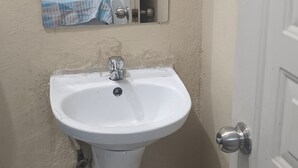 A small bathroom with a white sink, a mirror, and a door. - Luisandro (Punta Cana)