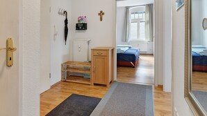 Une pièce avec un plancher en bois, un lit, un petit bureau, un radiateur, une fenêtre avec des rideaux et une porte à clé.