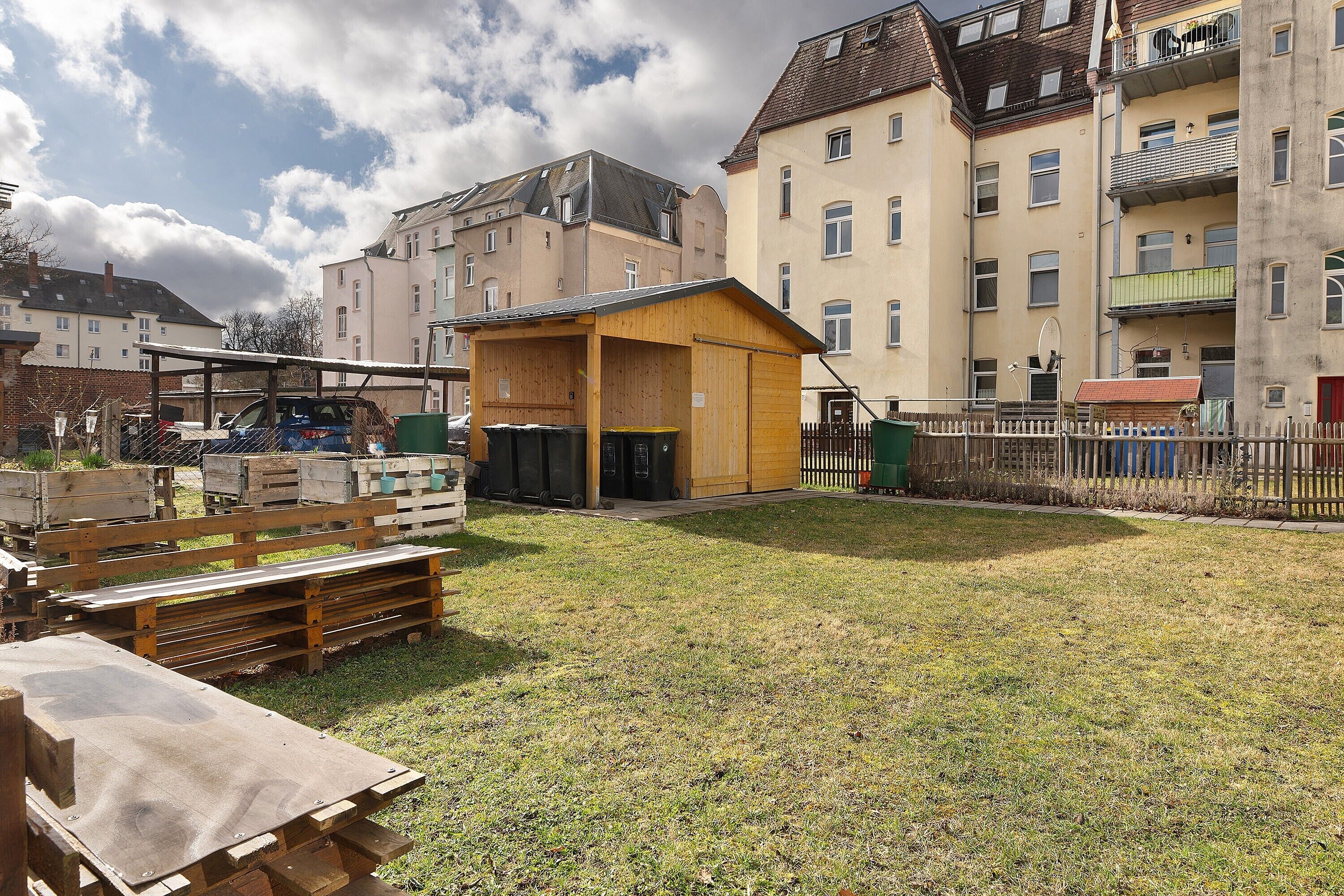 Un quartier résidentiel avec une petite construction en bois, une cour clôturée et, au fond, des immeubles à plusieurs étages.