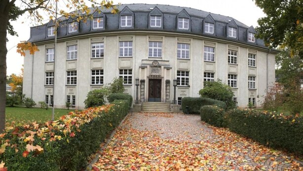 Un grand bâtiment historique à la façade symétrique, doté de nombreuses fenêtres et d’une entrée centrale.