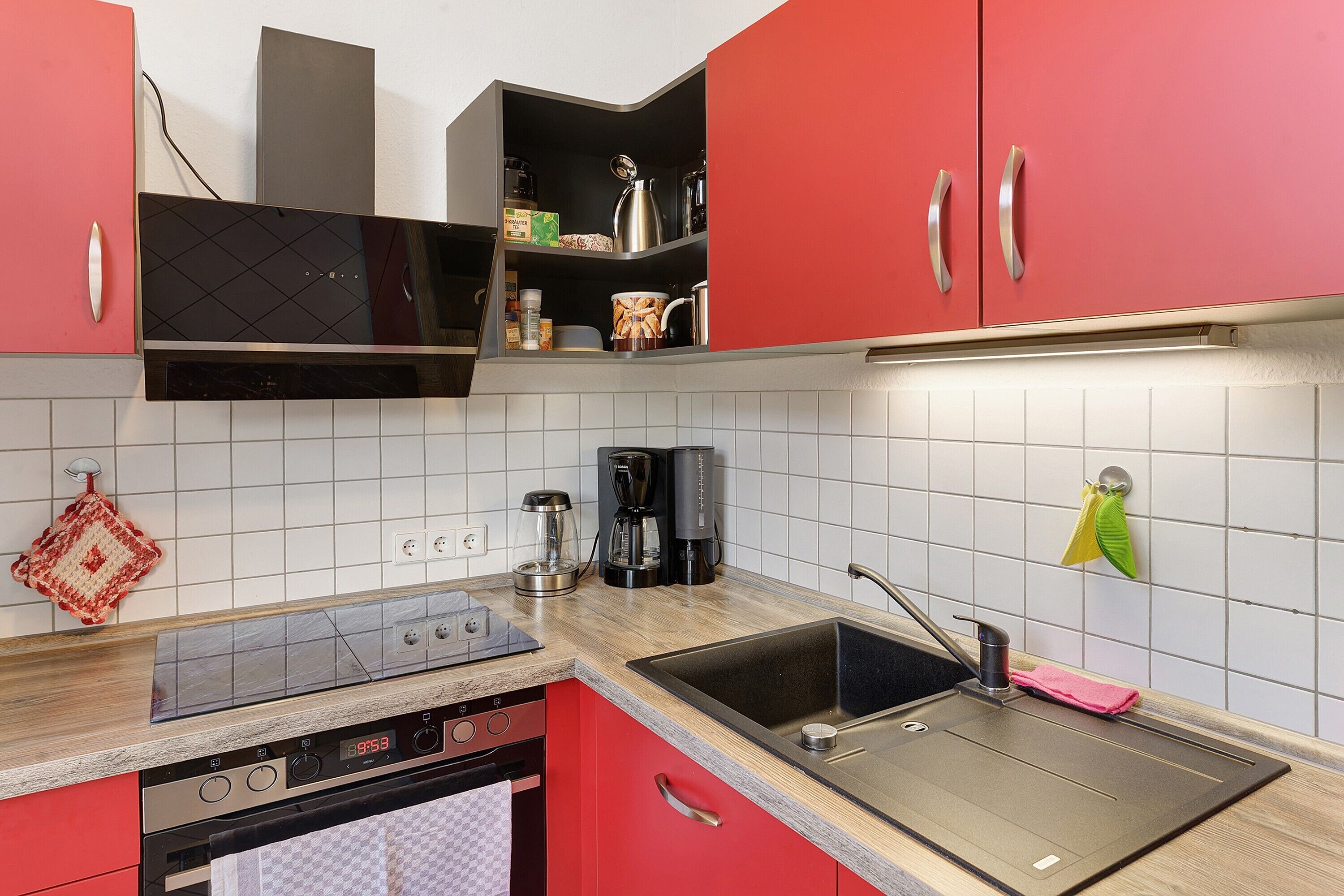 A kitchen with red cabinets, a stainless steel sink, a coffee maker, and a microwave.