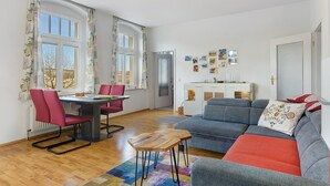 Un vaste espace de vie comprenant une table à manger, des chaises rouges, un canapé gris et un tapis coloré.