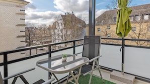 Un balcon avec une table en verre, une plante en pot et un parasol vert.