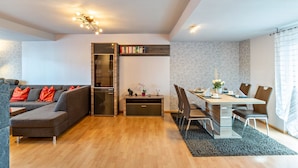 Ein modernes Wohnzimmer mit einer Eckcouch, einem Esstisch mit Stühlen, einer integrierten Küche und einem kleinen Beistelltisch mit Dekoration.