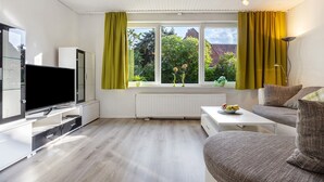 Ein modernes Wohnzimmer mit Flachbildfernseher, einer Couch, einem Couchtisch und einem Fenster mit Vorhängen.