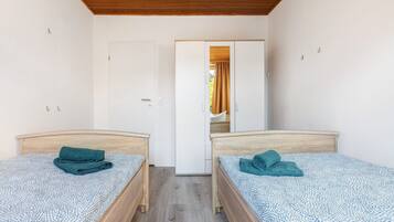 A room with two single beds, a wooden ceiling, white walls, and a door leading to another room.