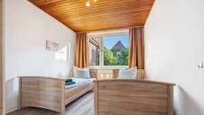 Ein Zimmer mit zwei Holzbetten, einem fenster mit Vorhängen, einer Holzbalkendecke und Blick auf Gebäude.