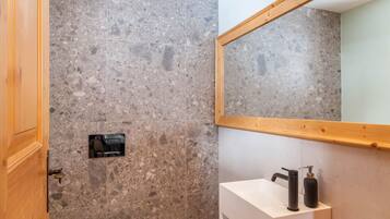 Un baño con pared de piedra, puerta de madera, lavamanos blanco, grifo negro y espejo.